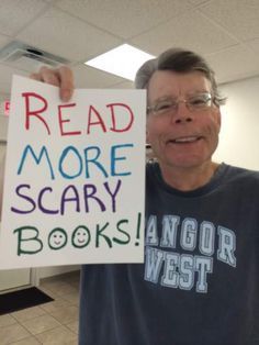 a man holding up a sign that reads read more scary books