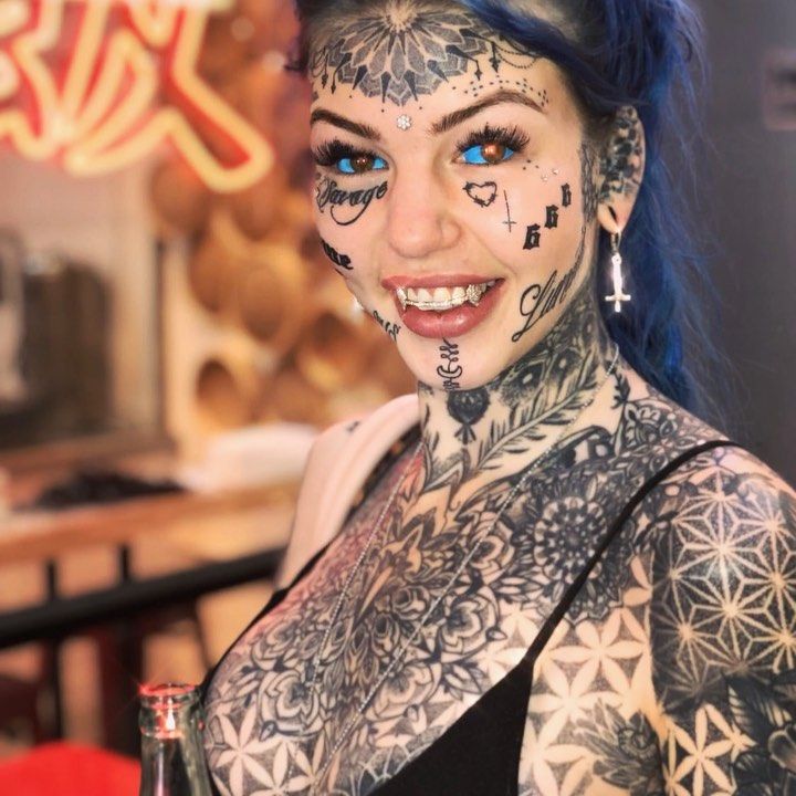 a woman with blue hair and tattoos on her face, holding a wine glass in front of her