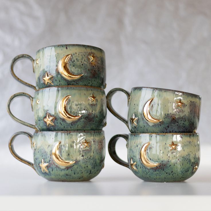 four coffee mugs with gold stars and moon designs on them sitting side by side