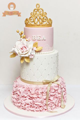 a three tiered cake with pink ruffles and gold decorations on it's side