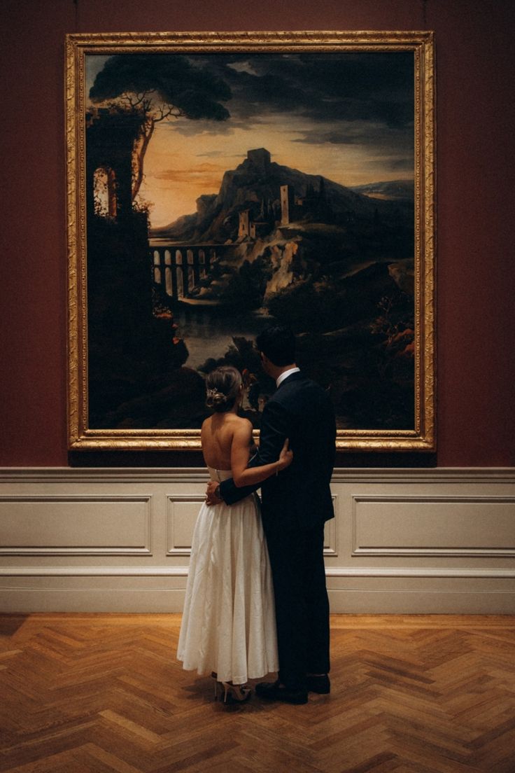 a man and woman standing in front of a painting on the wall with their arms around each other