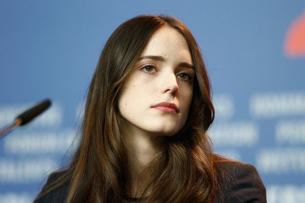 a woman with long brown hair is sitting in front of a microphone and looking off to the side