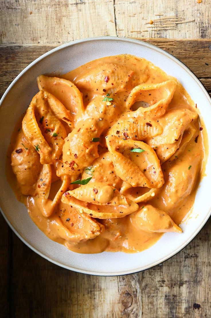 a white bowl filled with pasta covered in sauce on top of a wooden table next to a fork