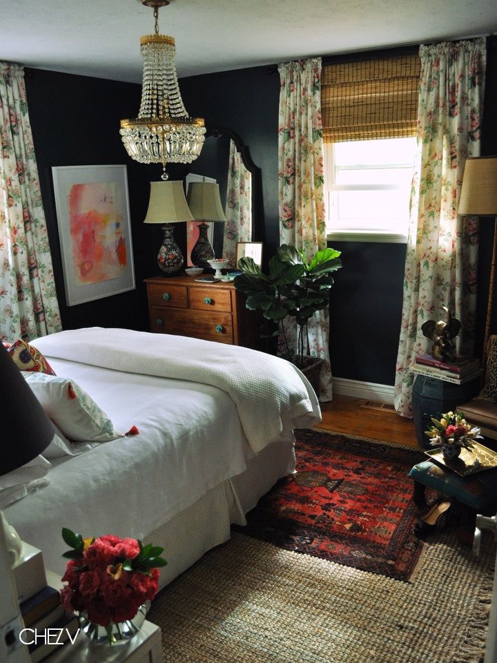 a bedroom with black walls, floral curtains and a chandelier hanging from the ceiling