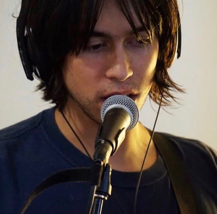 a man with headphones on singing into a microphone and holding a guitar in front of him