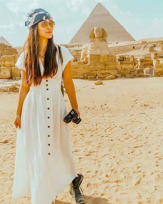 a woman standing in front of the pyramids with a camera and hat on her head