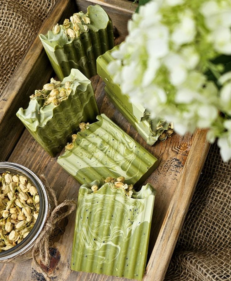 four green soap bars sitting on top of a wooden tray next to a bowl of flowers