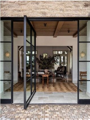 an open glass door leading to a living room and dining area with brick flooring