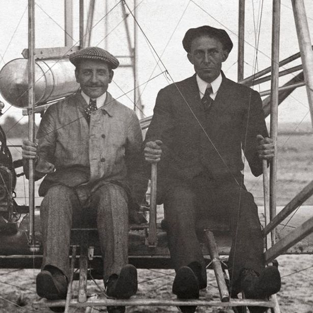 two men are sitting in an old fashioned biplane with one man holding a propellor