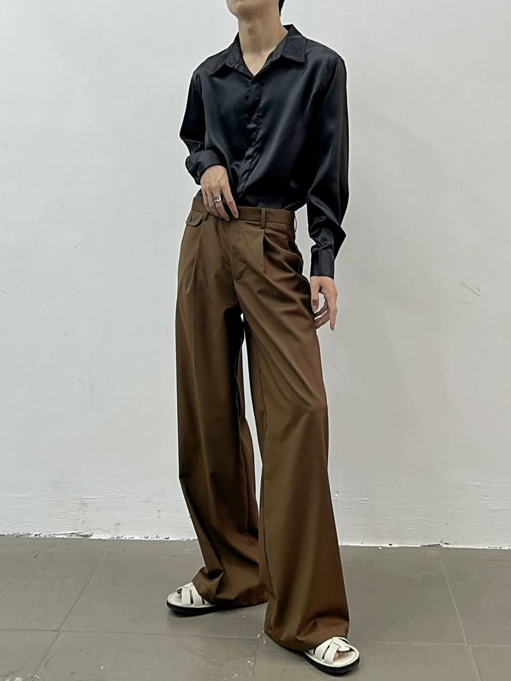 a woman standing in front of a white wall with her hands on her hips wearing brown pants