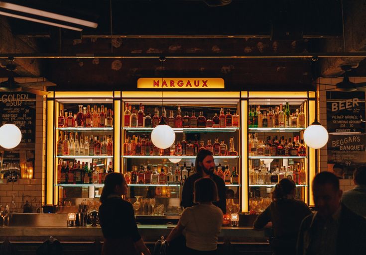 people are sitting at the bar in front of the liquor bottles on the shelves behind them