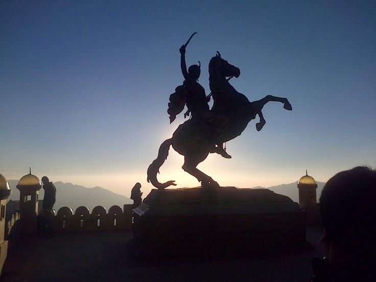 the silhouette of a statue of two people riding horses in front of a mountain range