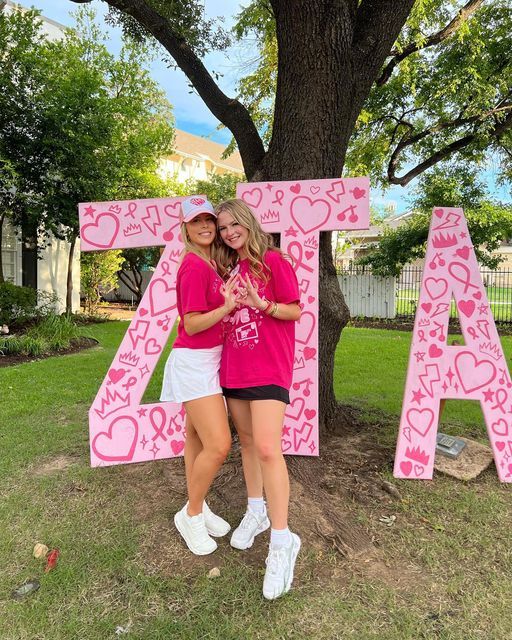 two girls standing in front of a large pink letter