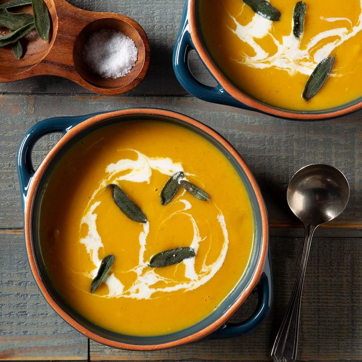 two bowls of pumpkin soup with sagel garnish and spoons on the side