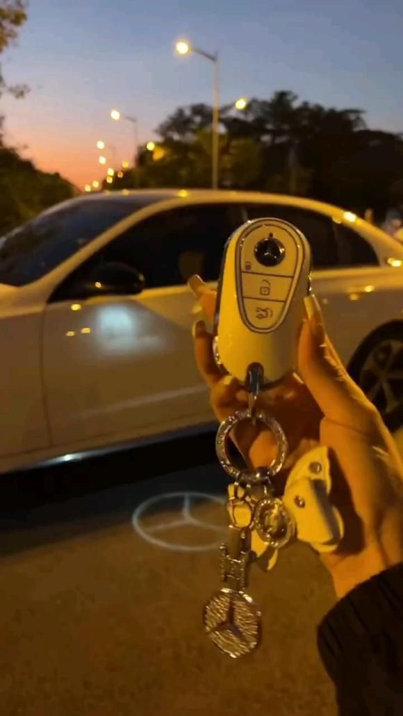 a person holding up a car keychain in front of a parked white car