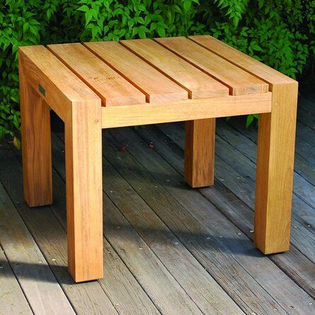 a wooden bench sitting on top of a wooden floor next to green bushes and shrubbery