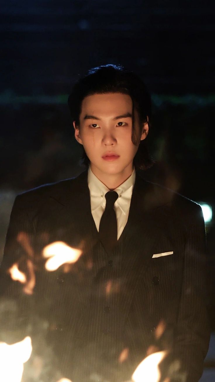 a young man in a suit and tie standing next to a bright light that is shining on him