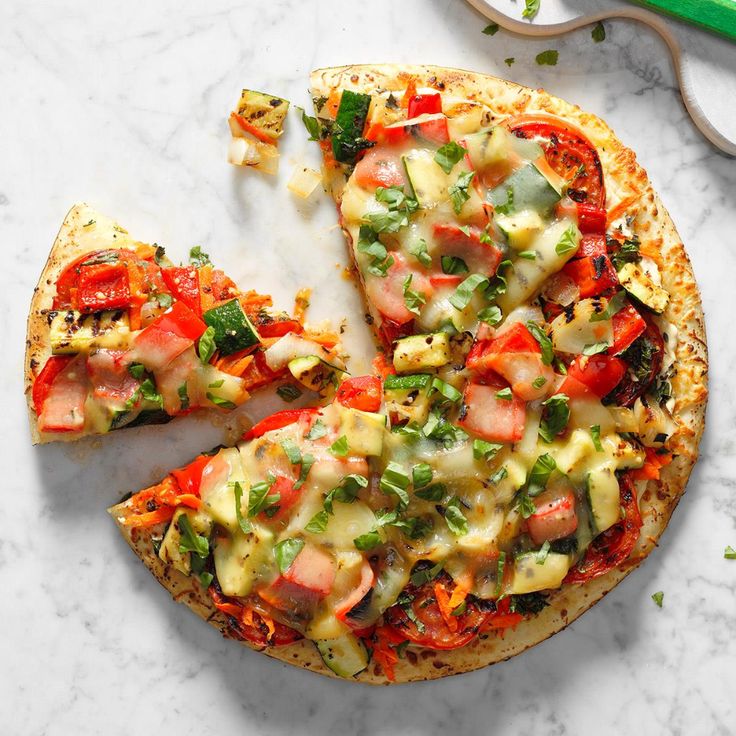 a pizza with several toppings cut into slices on a marble surface next to a green spatula