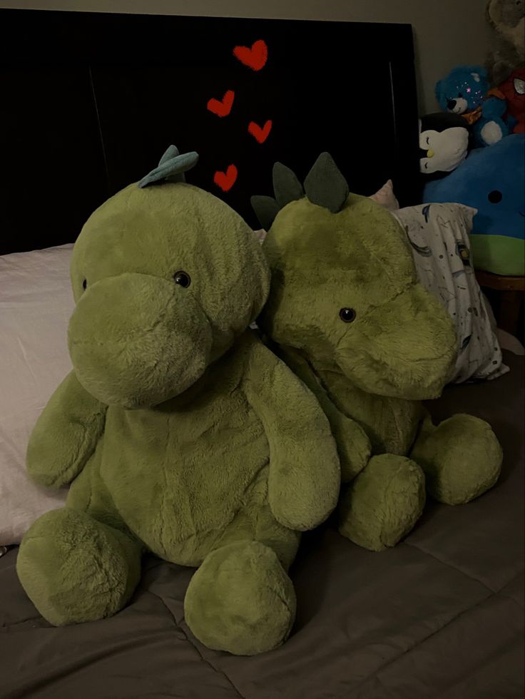 two green stuffed animals sitting on top of a bed next to each other in front of a black headboard