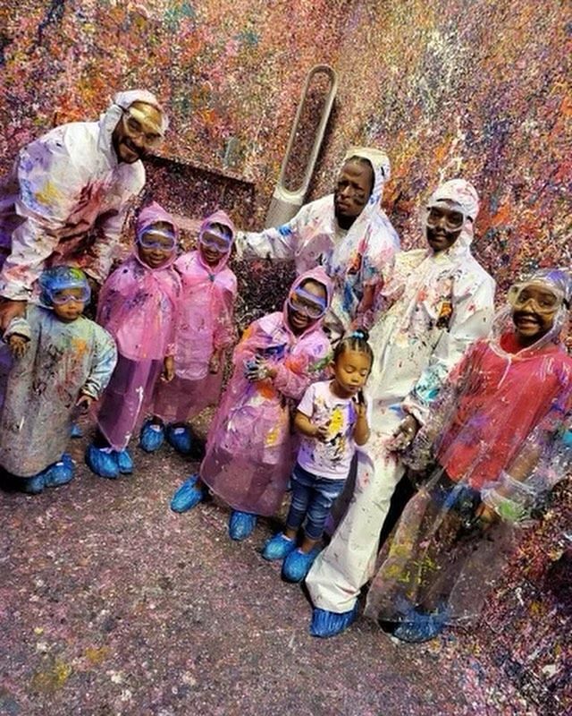 a group of people standing next to each other in front of a wall covered with colored powder