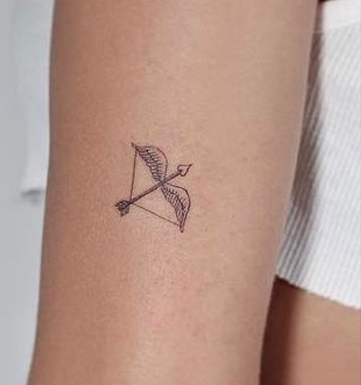 a woman's arm with a small bow and arrow tattoo on the left side