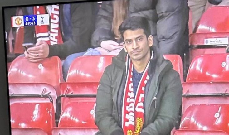 a man sitting in front of a tv screen with a scarf around his neck and hands on his knees