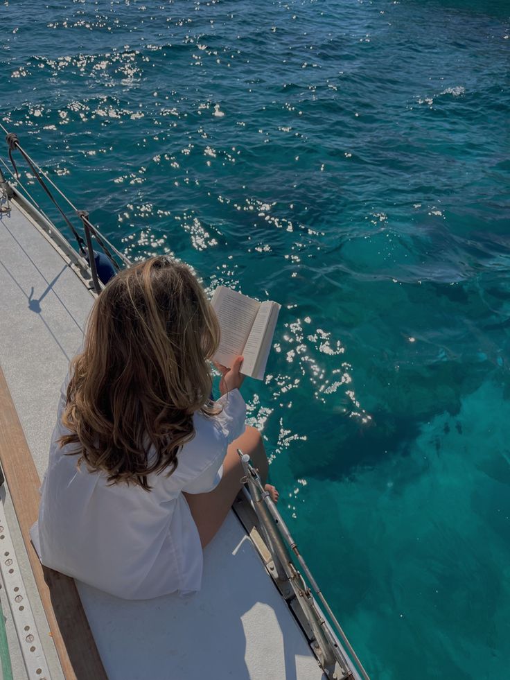 a person sitting on a boat in the water reading a book and looking at something