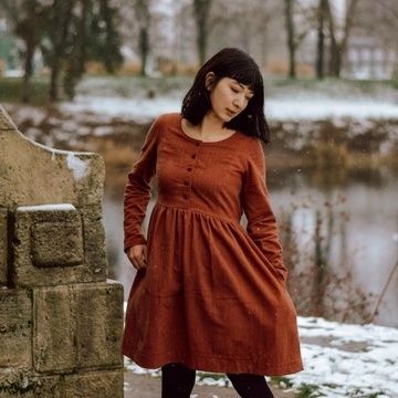 a woman is standing in the snow wearing a red dress and black tights with her hands on her hips