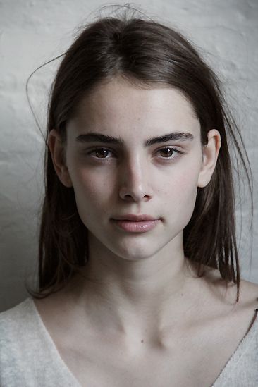 a young woman is posing for the camera in front of a white wall with her hair pulled back