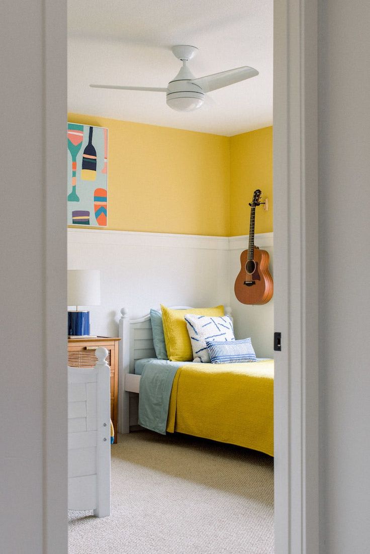 a bedroom with yellow walls and a guitar hanging on the wall next to the bed