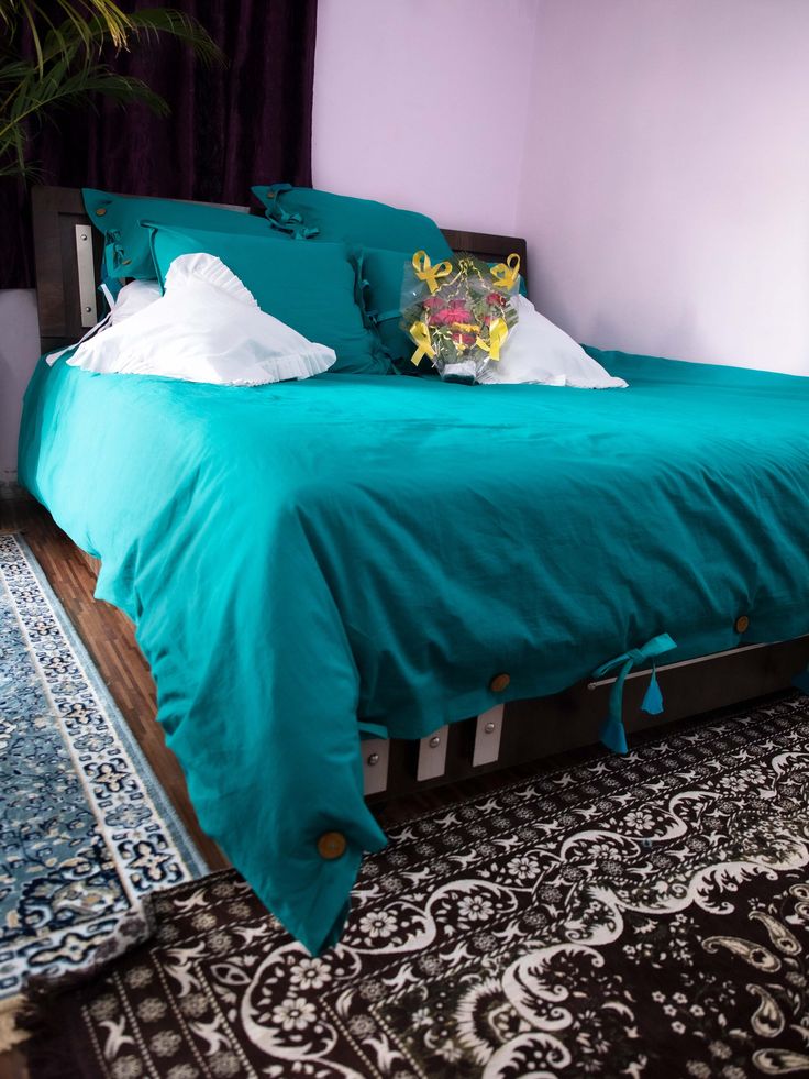 a bed with blue sheets and pillows in a room next to a rug on the floor