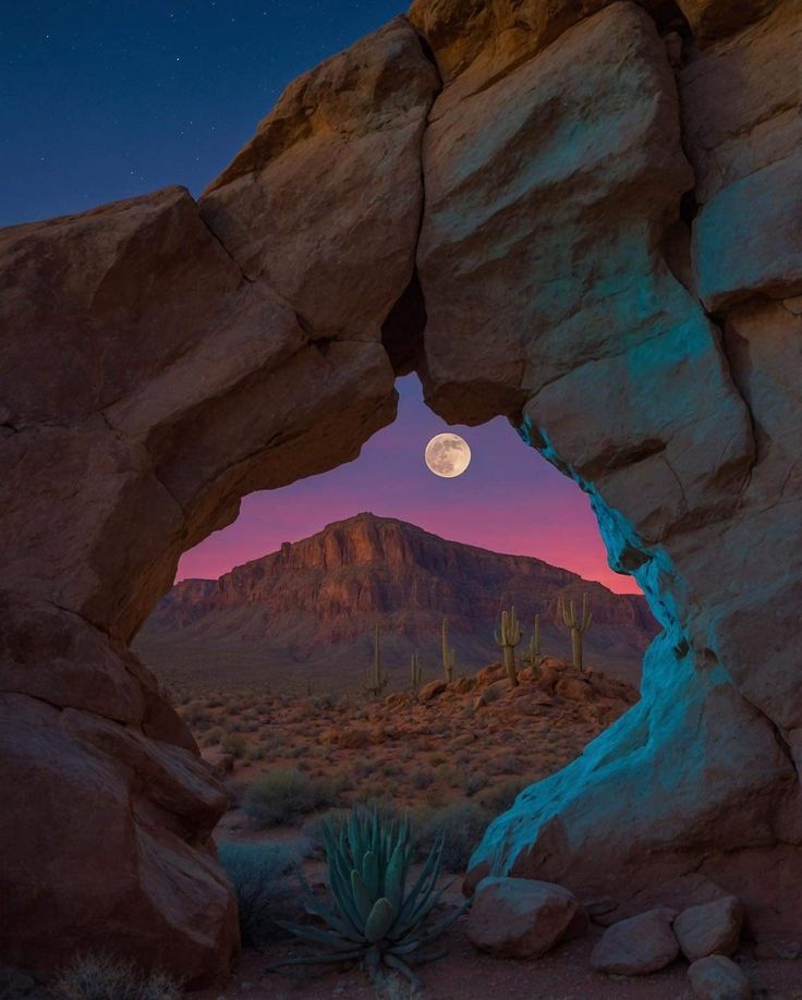 the full moon is seen through an opening in a rock formation with cactus and cacti