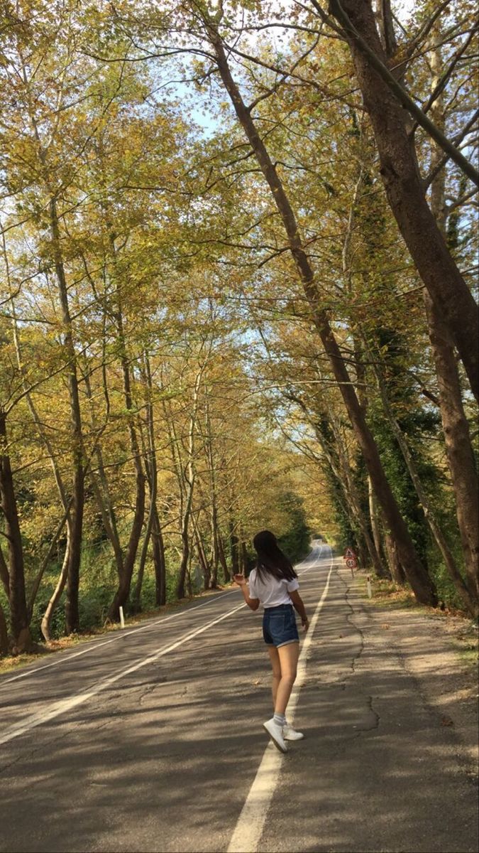 a woman walking down the middle of a tree lined road