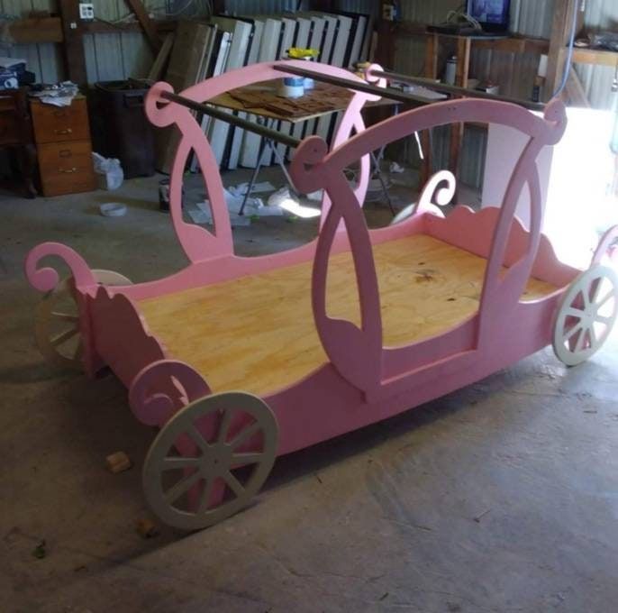 a pink wooden bed with wheels on the bottom and sides, sitting in a garage