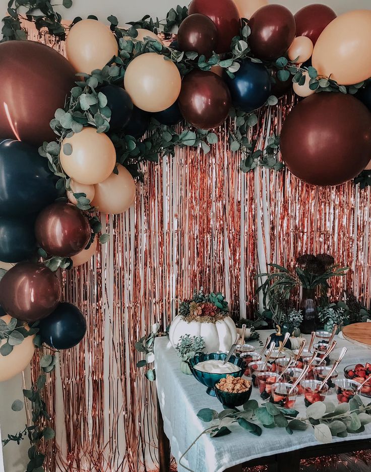 a table topped with lots of balloons next to a wall covered in foil streamers