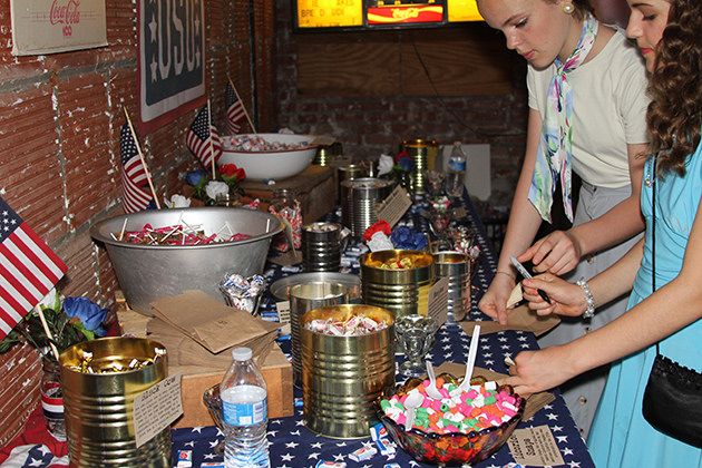 two girls are standing at a table with patriotic decorations on it and one girl is cutting into a cake