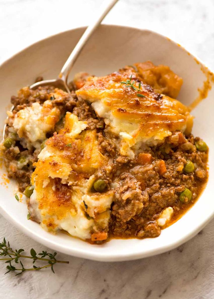 a white bowl filled with meat and cheese casserole on top of a table