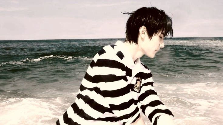 a young man sitting on top of a beach next to the ocean