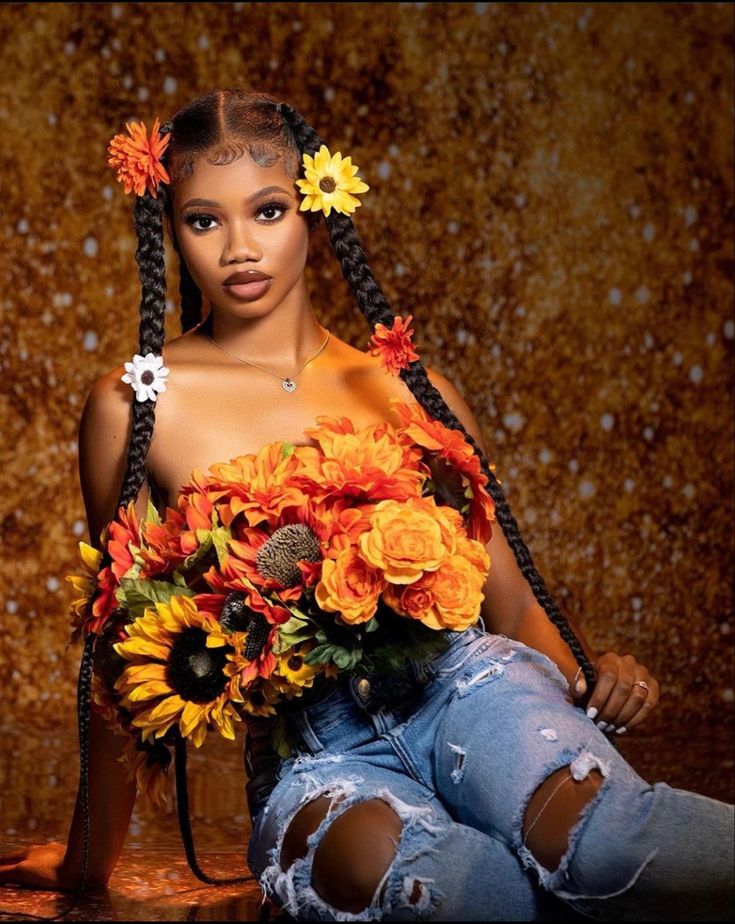 a woman with braids and flowers in her hair sitting on the ground next to a wall