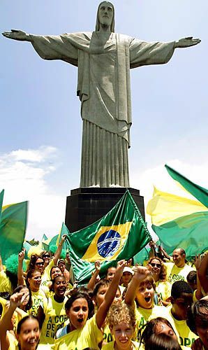 a group of people standing in front of a statue with flags around their necks and arms