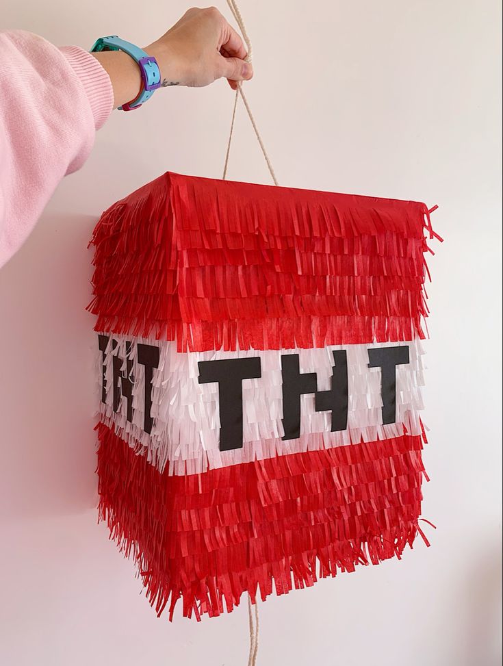 a person holding a red and white box with the word tht hanging from it