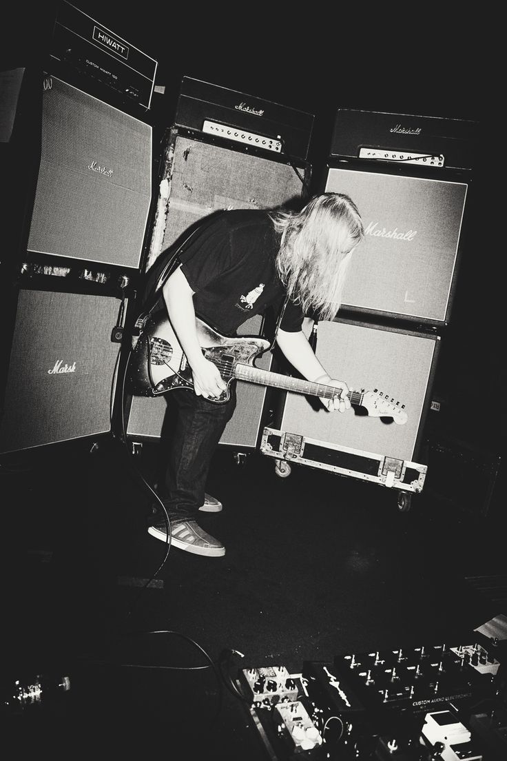 black and white photograph of a man playing guitar in front of sound equipment on stage