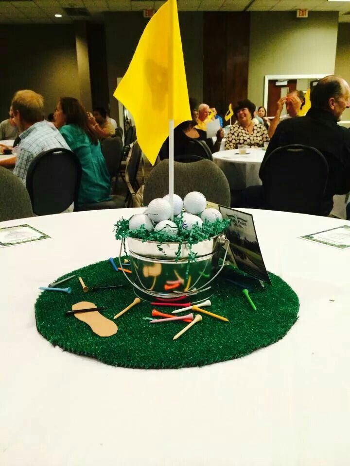 a golf themed centerpiece on top of a round table with people in the background