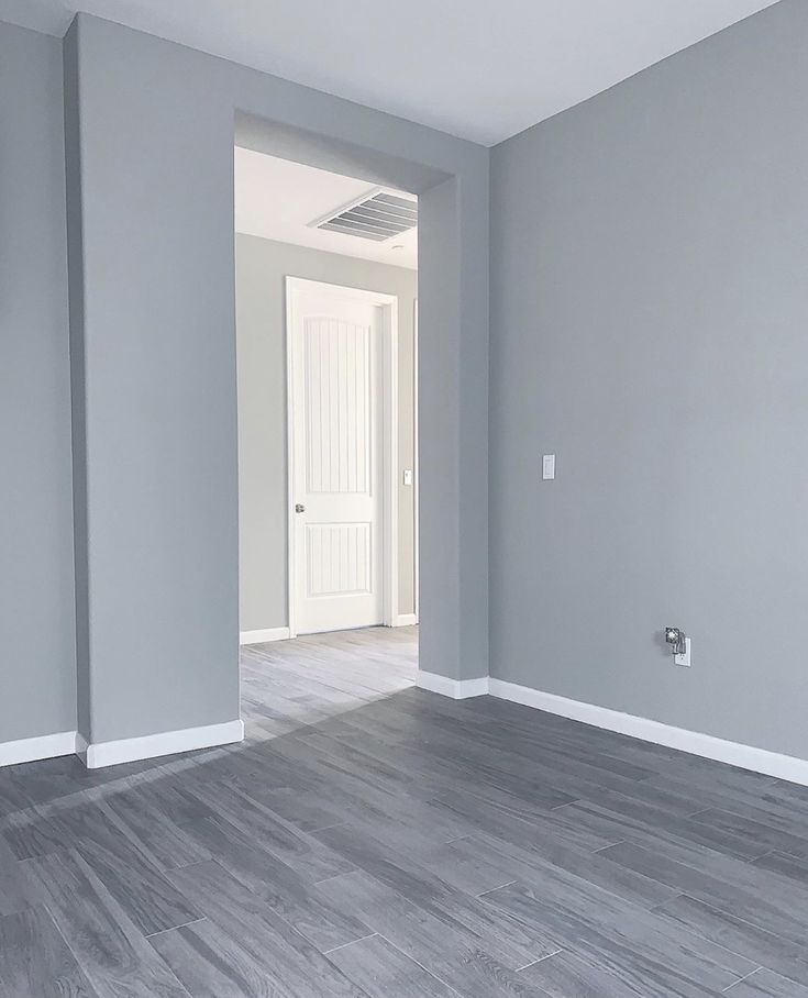 an empty room with gray walls and wood flooring in the foreground is a white door