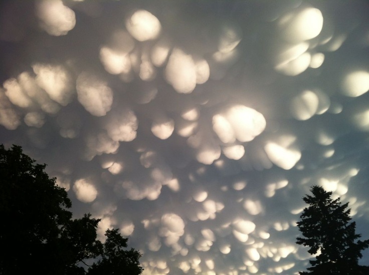 the sky is filled with many clouds and some trees in front of it at night