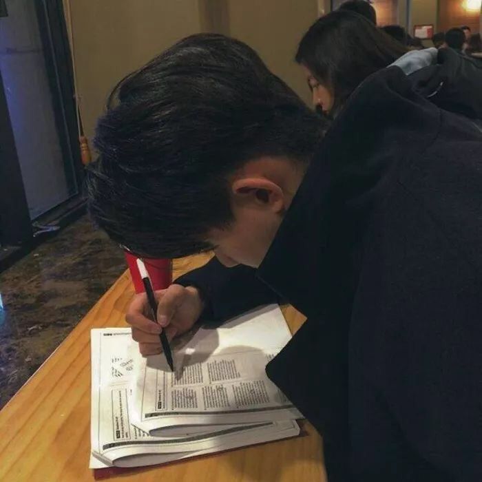 a young man writing on top of a piece of paper with a pen in his hand