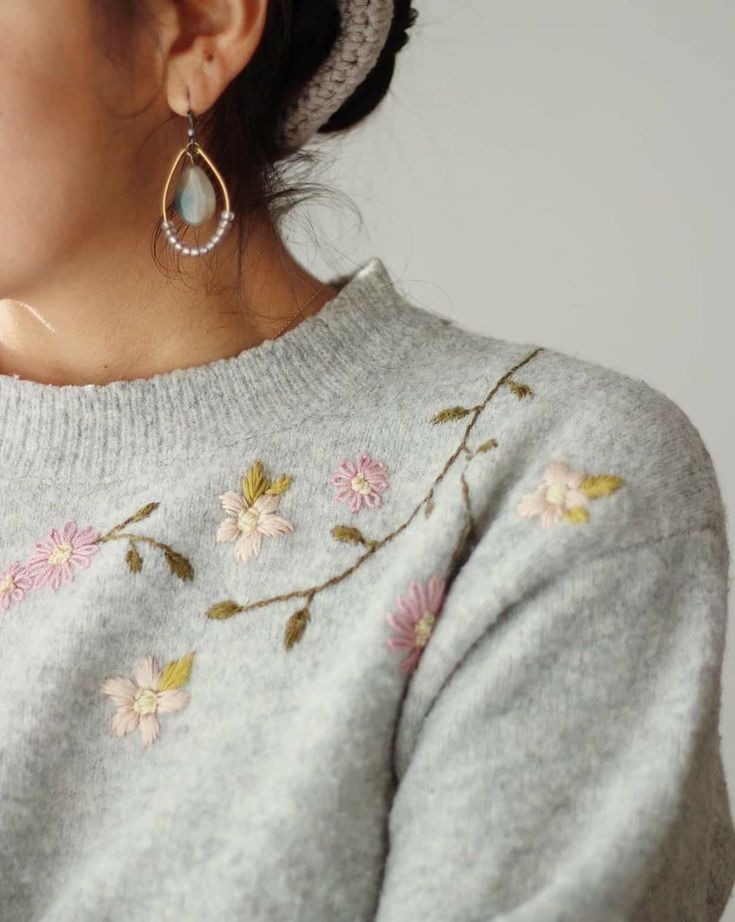 a close up of a person wearing a sweater with flowers on it and a pair of earrings