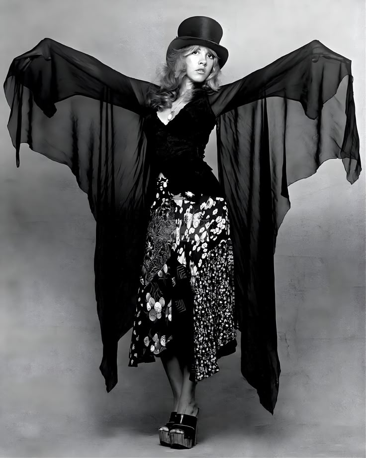 a woman in a black dress and hat with her arms outstretched