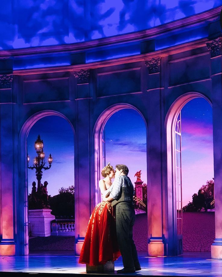 a man and woman dance on stage in front of archways at night with purple lighting