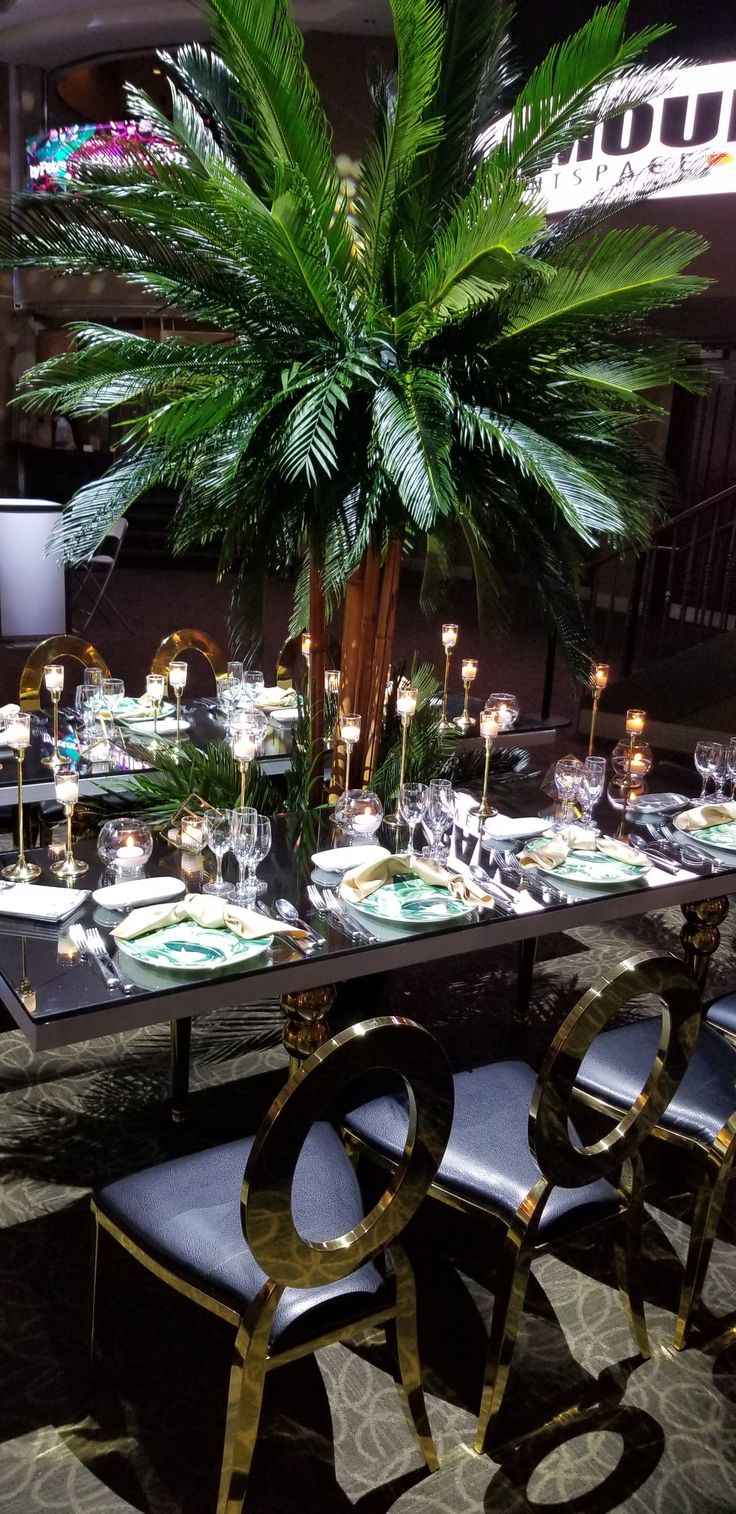 a table set up with place settings and palm tree in the center for an event